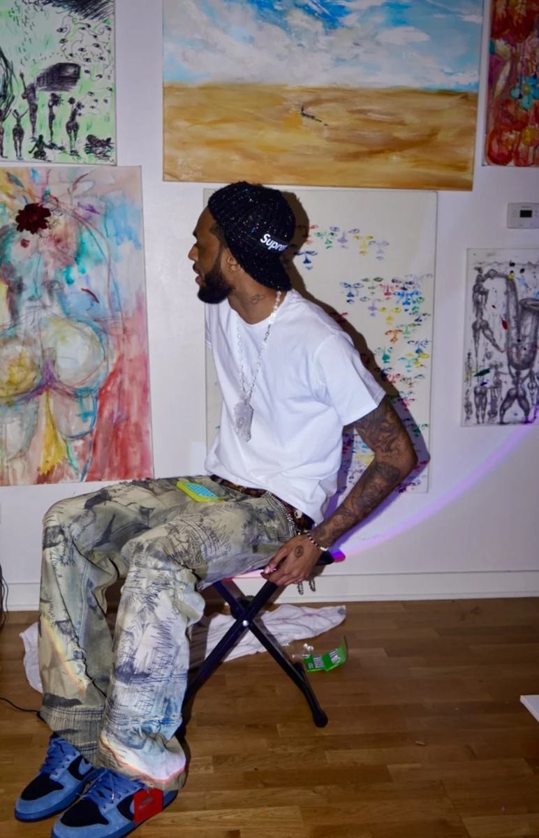 Justin White Foreva sitting in his studio surrounded by his paintings
